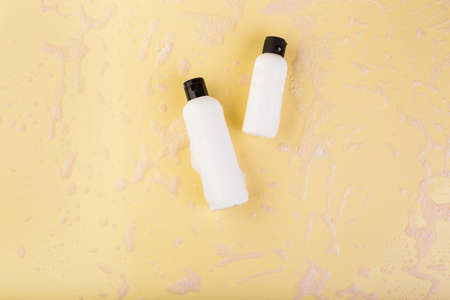 Two plastic bottles of different size on light yellow. No label. Close up, top view, copy space for...