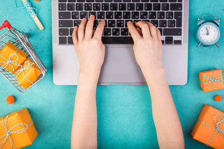 Female hands with laptop and orange presents on blue table flat lay. Holiday online shopping concept.の写真素材