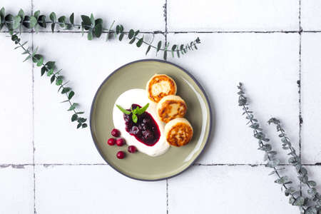 Cottage cheese pancakes, syrniki with fresh berries and jam for breakfast on tile with eucalyptusの写真素材