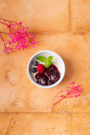 fancy panna cotta with berries jam and mint on brown background pink flowers