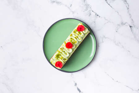 Pastry cake dessert decorated with green cream, cherry and pistachio on marble backgroundの写真素材