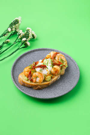 Toast with shrimp, prawns, avocado and poached egg on green background with flowersの写真素材