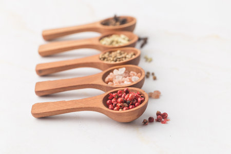 Various spices and green herbs in wooden spoons on white tableの写真素材