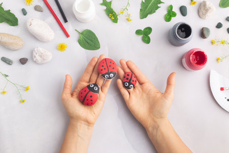 Drawing a ladybug on a stone with acrylic paints. Home hobbies are authentic. Artwork on stones. Woman hands.の写真素材