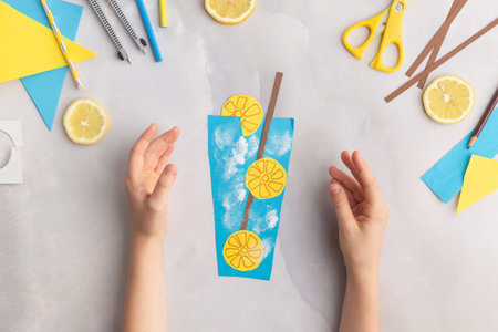 Paper lemonade with lemons. Children at home. Hands making DIY summer crafting. Kindergarten ideas step by step.の写真素材