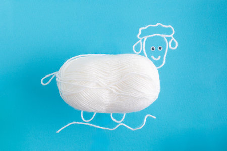 Drawing of sheep from wool threads with ball integrated knitting creative concept flat lay on blue