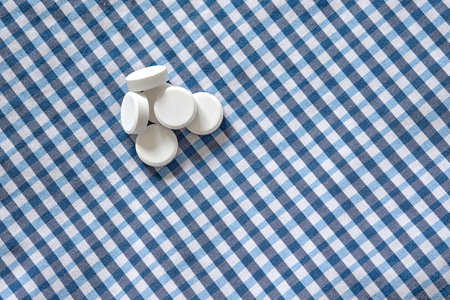A pile of round pharmaceutical medicine drugs tablets on a white-blue checkered textile cloth. Top...