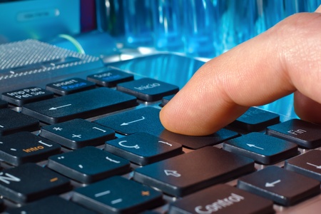 finger pressing the Enter key on a laptop with blue tubes in the background