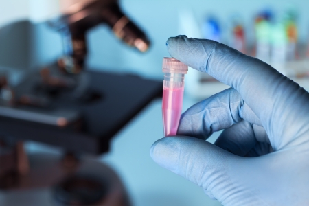 hand holds a test tube filled in with a pink liquid and microscope in backgroundの写真素材