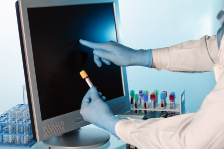 lab technician with a tube of blood in hand referring to the touch screenの写真素材