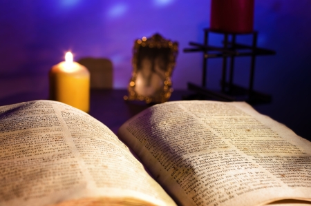 An open old book illuminated by candlelight and various ancient objects in backgroundの写真素材