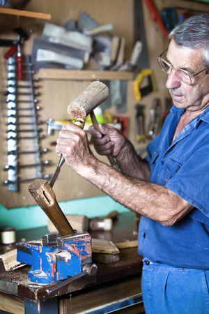 carpenter in the workshop garage handling a chisel and a hammer on a piece of woodの写真素材