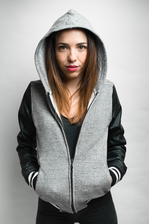 Portrait of young woman in hip hop style with his hands in his jacket pockets and hood on his head on gray background / girl urban hiphop style looking at cameraの写真素材
