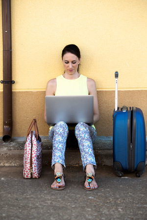 beautiful girl sitting on the street with your laptop and suitcases waiting for traveling  Pretty travelling woman consulting a travel destination for your holidaysの写真素材