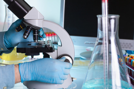scientist looking through a microscope with screen in background in the lab