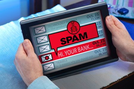 man with tablet which see emails and alert message with the word Spam  hands of a man looking inbox in tablet with a Spam messageの写真素材