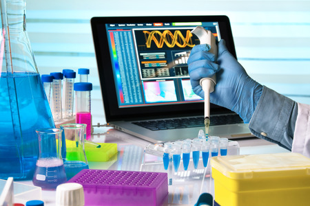 scientist holding dropper and working with laptop in genetics lab / researcher hands working with pipette and tubes in the laboratory tableの写真素材