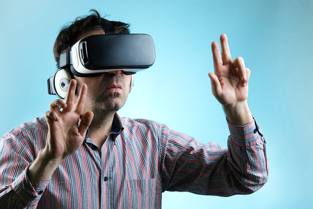 Adult Man Playing game with virtual reality device on a blue background / Man using virtual reality glasses and pointing with hands  の写真素材