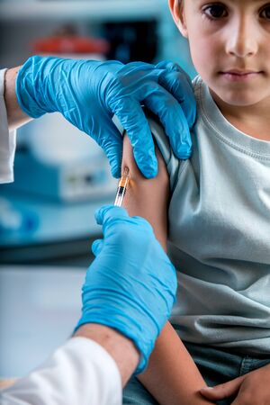 doctor vaccinating child in the pediatric clinic / pediatrician injecting a subcutaneous vaccine to...