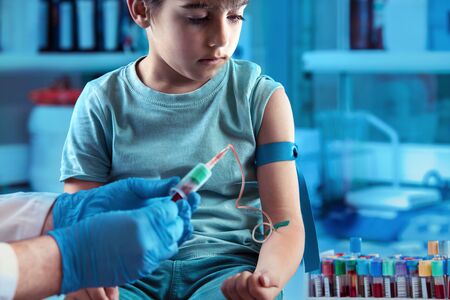Doctor taking blood sample test of a little boy in the clinic / technician making blood tests on a young boy in the laboratory of blood extractionsの写真素材