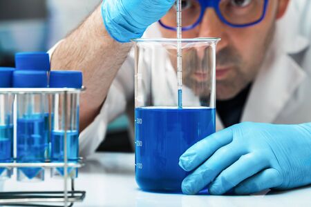researcher in the lab with material of analysis of substance liquids / Scientist holding beaker with blue liquid for analysis of fluids in the labの写真素材