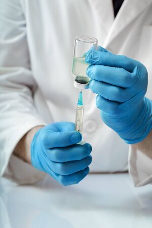 practitioner filling a syringe with an injectable vaccine / doctor preparing medication for the vaccination campaignの写真素材