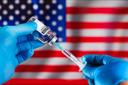 Doctor preparing a vaccine injection for the annual vaccination campaign against diseases in the USA. Preparation of a dose of vaccine in a syringe with a vial of the antibiotic and in the background the flag of the EEUUの写真素材