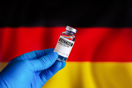vial of vaccine for the vaccination plan against diseases in the Germany. Doctor with a vial with doses of the vaccine in front of the Germany flagの写真素材