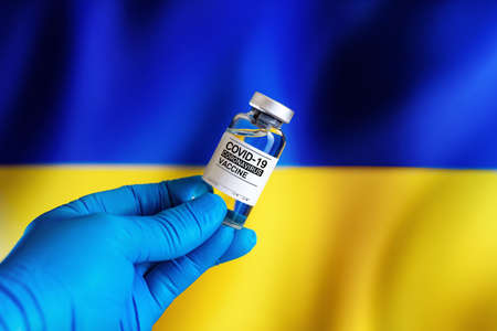 Doctor with vial of the vaccine for covid-19 and Ukrainian flag in the background. vial of vaccine for the vaccination against coronavirus plan in Ukraineの写真素材