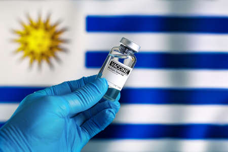 Doctor with vial of the vaccine for covid-19 and Uruguay flag in the background. vial of vaccine for the vaccination against coronavirus plan in Uruguayの写真素材