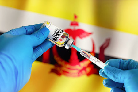 Doctor preparing vial of vaccine injection for the vaccination plan against diseases in Brunei. Injecting dose of vaccine in syringe for infections prevention in front of the Brunei flagの写真素材