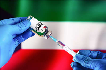Doctor preparing vial of vaccine injection for the vaccination plan against diseases in Kuwait. Injecting dose of vaccine in syringe for infections prevention in front of the Kuwait flagの写真素材