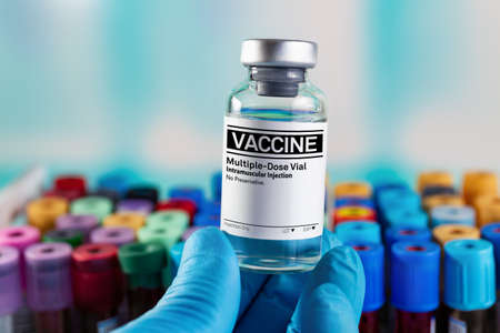 Researcher's hand with generic vaccine vial for the vaccination program against infectious disease prevention. doctor holding generic Vaccine vial and in background tray with tubes of blood samplesの写真素材