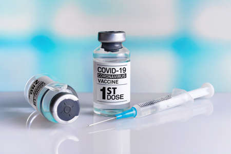 Coronavirus vaccine bottle with the name of the First dose of vaccine on the label. Covid-19 Vaccine Vials for vaccination of population tagged with 1st doseの写真素材