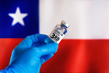 third dose vaccine for Covid-19 for booster shot in the risk population diseases in Chile. Doctor with a vial with 3rd dose of the vaccine for covid-19 or Coronavirus in front of the Chile flagの写真素材