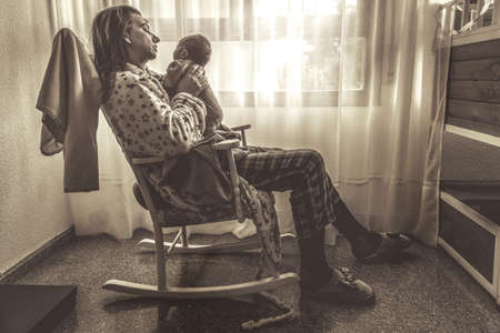 Young mother holding her newborn child. Mom nursing baby. Woman and new born boy relax in a white bedroom with rocking chair and blue crib. Nursery interior. Mother breast feeding baby. Family at homeの写真素材