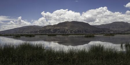 Reed, lake, mountains and clouds with reflection in the lake Titicaca, Peruの写真素材