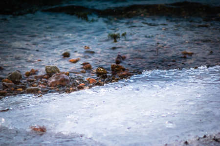 River waves on frozen shore of small stone.の写真素材