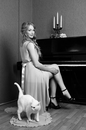 sexy beautiful blonde girl in dress playing piano with a catの写真素材