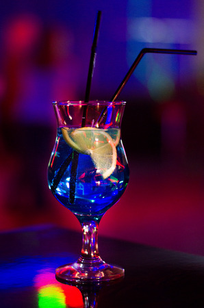 Beautiful glass with a cocktail at the bar on the table. Night club. Alcoholic drink blue color with a lemon on the insideの写真素材