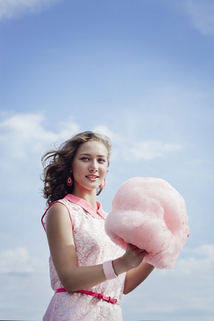 beautiful young blonde girl eats cotton candy in the summer on a blue sky background.の写真素材