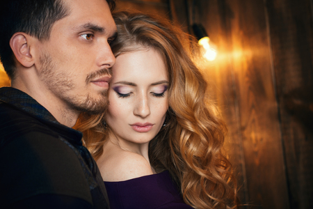 Beautiful couple in love hugging against the background of glowing lights. Studio portrait photo of a girl blondes and a guy with short hair. Valentine's day. Loving married couple. Family happinessの写真素材