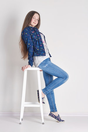 Russia Ekaterinburg - April 1, 2016: Young girl child sitting on a chair. Smile joy emotions on her face. Girl in jeans posing on light background. Summer lookのeditorial素材