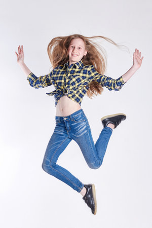 Russia Ekaterinburg - April 1, 2016: Cheerful Girl in shirt and jeans jumps on a white background, art fashion. Model school for children. Beautiful baby smilingのeditorial素材