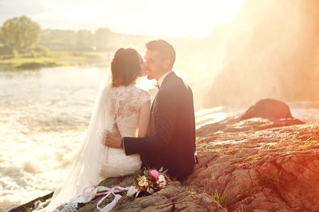 Beautiful couple love kissing while sitting on rocks near river. Wedding couple at sunset and rivers, love and tender feelings. Loving couple resting. Wedding ceremony outdoors. Perfect couple blurredの写真素材