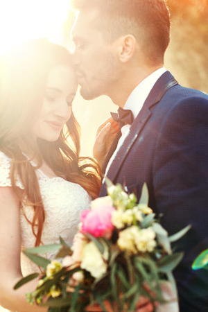 Couple hugging at sunset, lovers couple kissing in sunset. Wedding ceremony outdoors. Beautiful bride and groom with bouquet of flowers. White wedding dress for bride. Love wedding couple hug. Blurredの写真素材