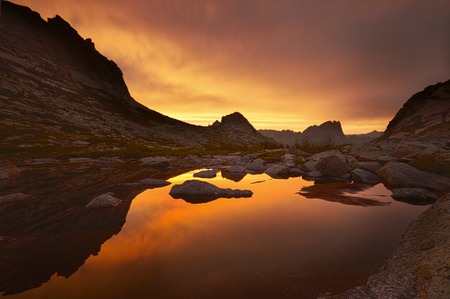 Sunset in mountains near lake. Sunlight reflected on mountain tops. Golden light from sky reflected in a mountain lake. Ergakiの写真素材