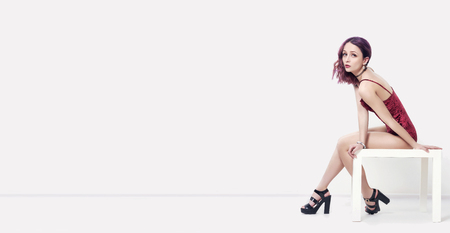 Mockup. Sexy woman with purple hair in lingerie sitting on the table and posing. Woman on a white background. Fashion art portrait of attractive sexy girlの写真素材