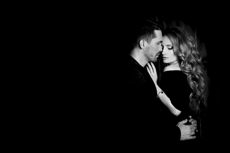Beautiful couple in love hugging against black background. Studio black and white portrait photo of a girl blondes and a guy with short hair. Valentine's day. Loving married couple. Family happinessの写真素材