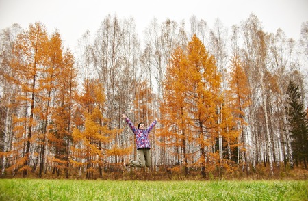 Woman rejoices at the arrival of autumn. Girl in a field near the yellow autumn forest, autumn came, the emotion of joy. Golden yellow trees in the forest. Birch groveの写真素材